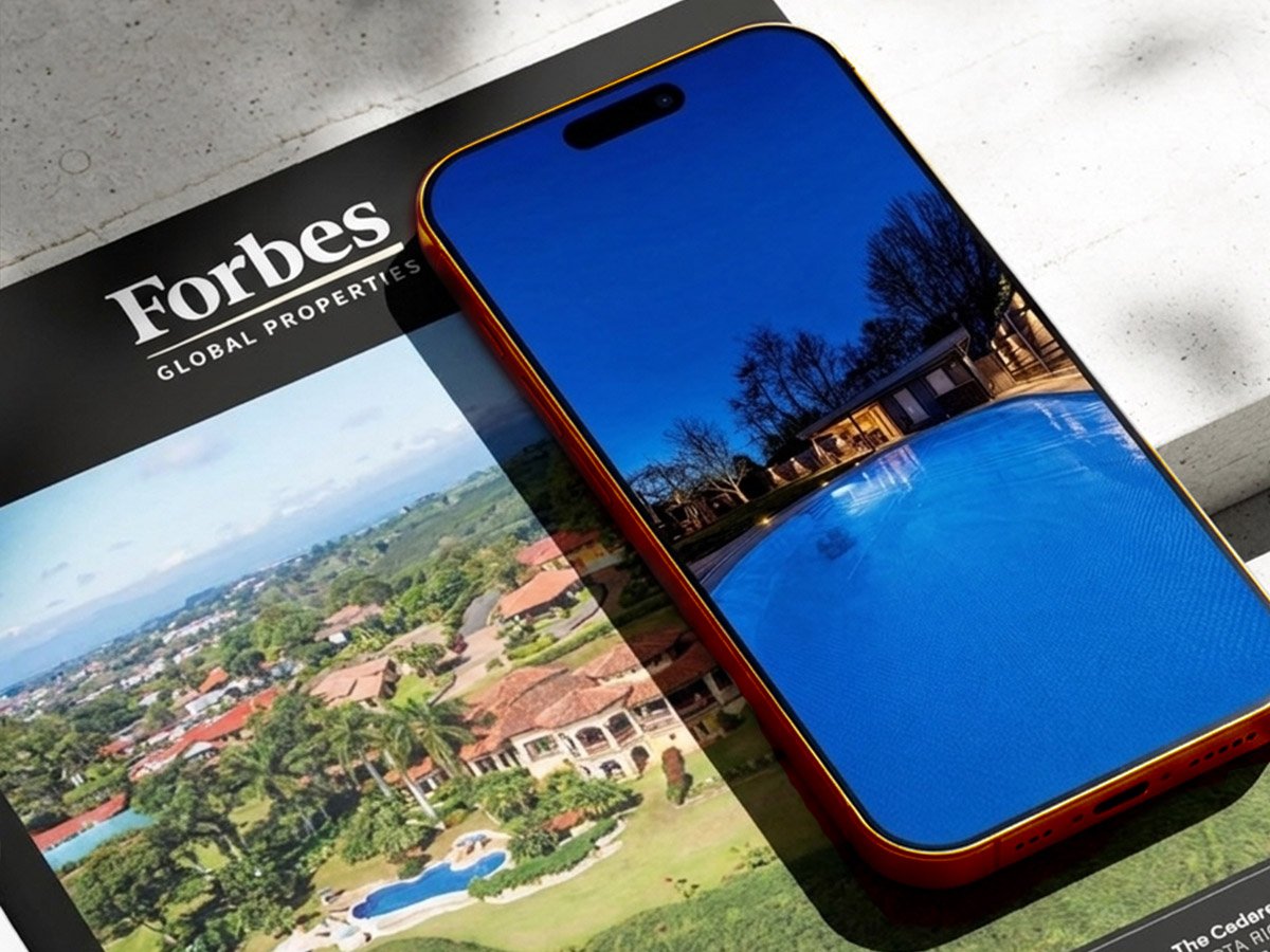 Forbes Global Properties &ndash; Immobilien-Content: Villa mit beleuchtetem Pool auf dem Smartphone über einem Forbes-Expos&eacute;
